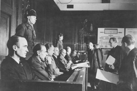 Schwarz-Wei&szlig;-Aufnahme eines Gerichtssaals beim N&uuml;rnberger Krupp-Prozess. Links sitzen mehrere angeklagte M&auml;nner in einer langen Bankreihe, davor und daneben stehen Milit&auml;rangeh&ouml;rige. Rechts sind Juristen mit Akten zu sehen. Der Raum wirkt dunkel, streng und konzentriert.