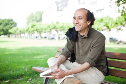 Der K&uuml;nstler Josef Schoenen sitzt auf einer Bank und h&auml;lt ein Buch in der Hand.