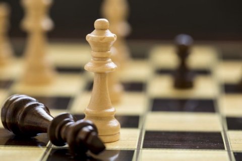 Schachbrett mit einem querliegenden schwarzen "K&ouml;nig" (Spielfigur) und eine dar&uuml;ber stehenden wei&szlig;en "Dame" (Spielfigur). Im unscharf gehaltenen Hintergrund befinden sich noch weitere Spielfiguren. 