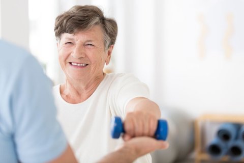 Eine Seniorin macht unterst&uuml;tzte &Uuml;bungen mit einer kleinen blauen Hantel. 